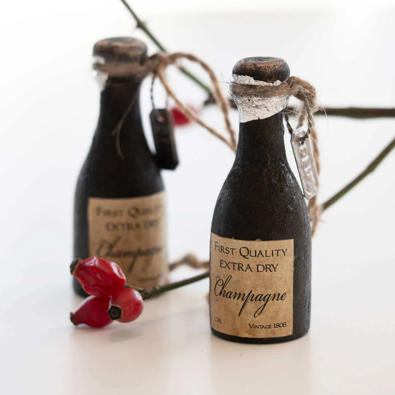 Two miniature champagne bottles with decorative labels on a white surface.