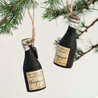 Two champagne bottle ornaments hanging from a tree branch.