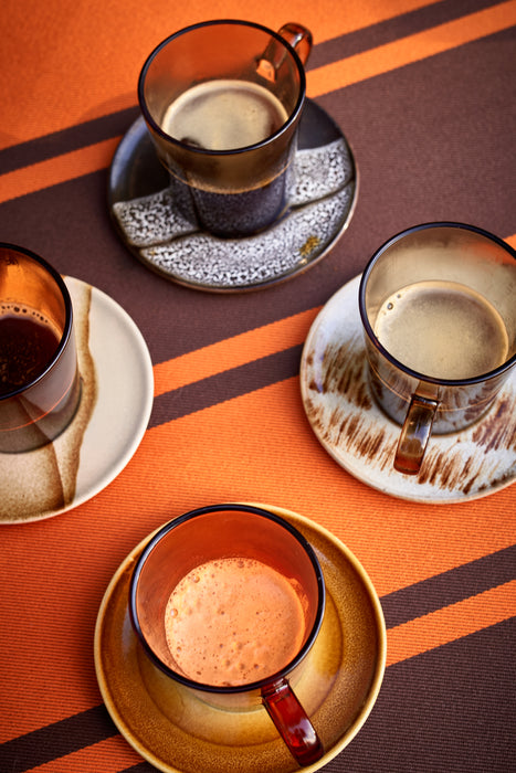 colored glass coffee cups with ear on ceramic saucers on orange and brown striped table