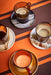colored glass coffee cups with ear on ceramic saucers on orange and brown striped table