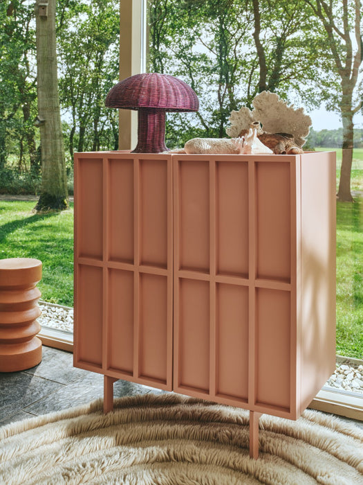 purple table lamp made from rattan on a blush colored credenza in front of a window