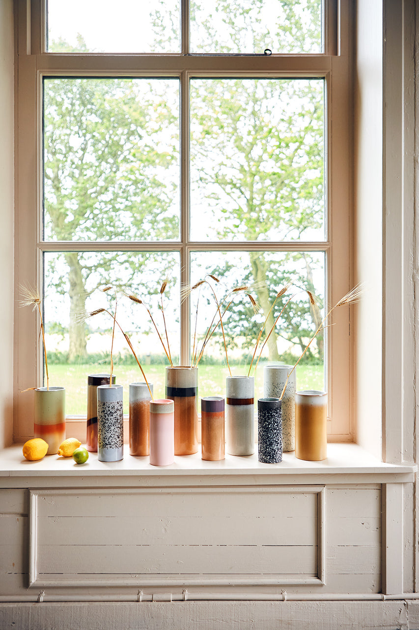 Retro style flower vases in a variety of colors lined up in a window that looks out over trees