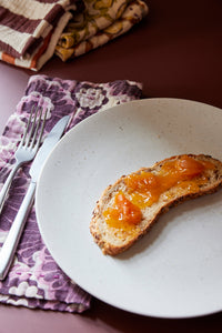 large, white speckled dinner plate with slice of bread and purple flowered napkin