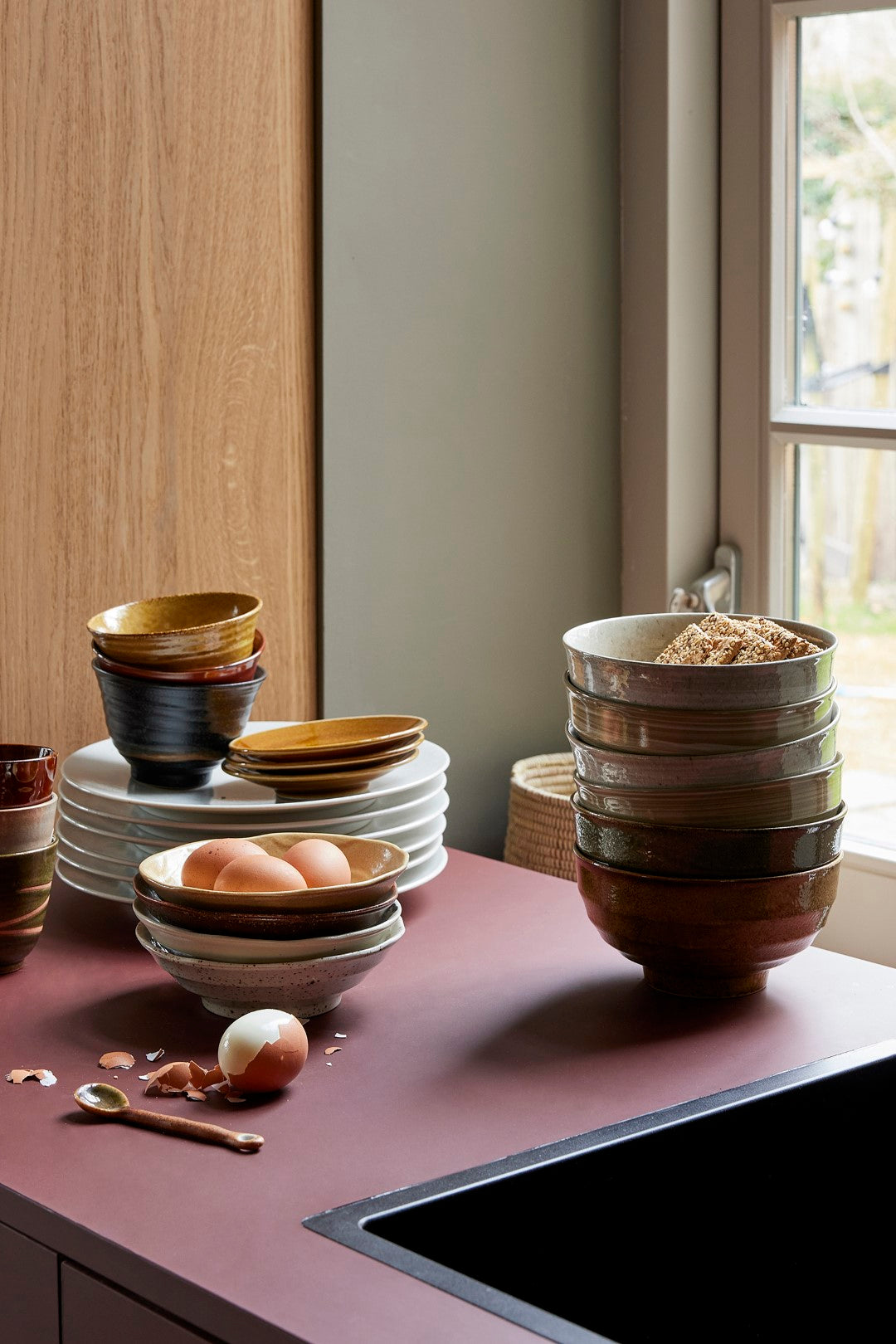 purple counter top with stack of white speckled dinner plates and stack of bowls in earth tones