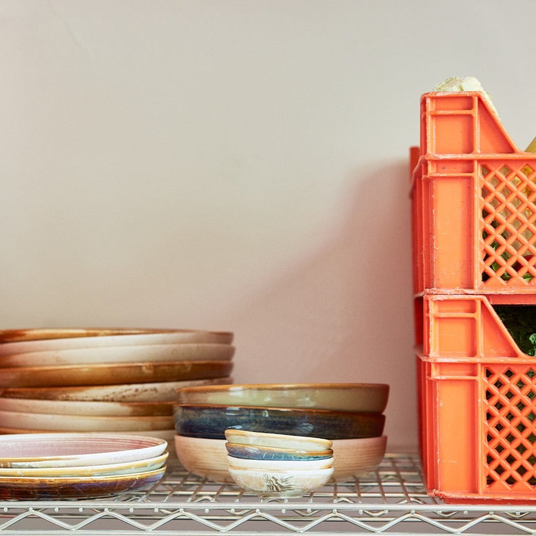 deep plates in green blue and cream on open shelving next to orange crate