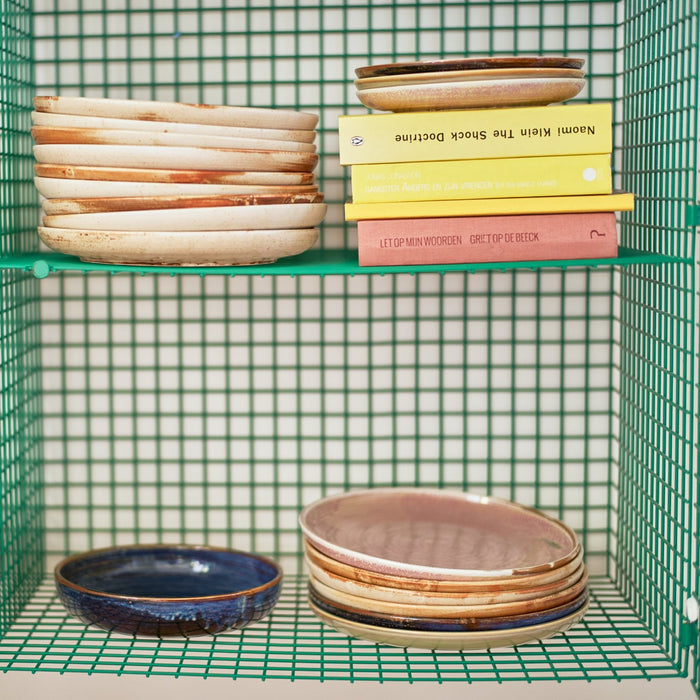stack of chef ceramics dinner lates in cream, pink and blue in a green open shelving unit