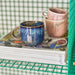 blue mug with ear in green shelving rack on a stack of magazines