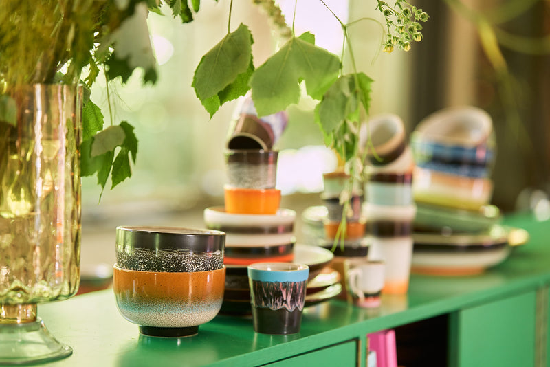 Colorful ceramic cups and bowls on a green surface with blurred background
