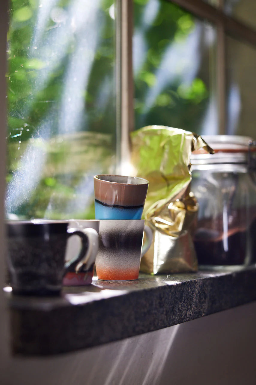 4 different colored retro style espresso cups with ear  on a shelf with a pack of coffee