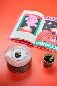 retro style black and pink cookie jar on an orange table top with coffee mug and magazine