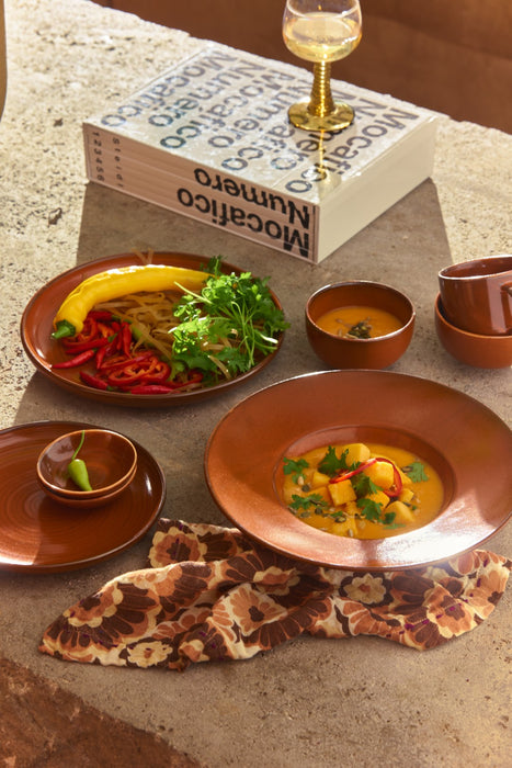 small ceramic bowl orange color on table with book and food on plates