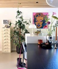 living room with art work in pink, beige set of drawers and blue shiny vase with flowers on a black table