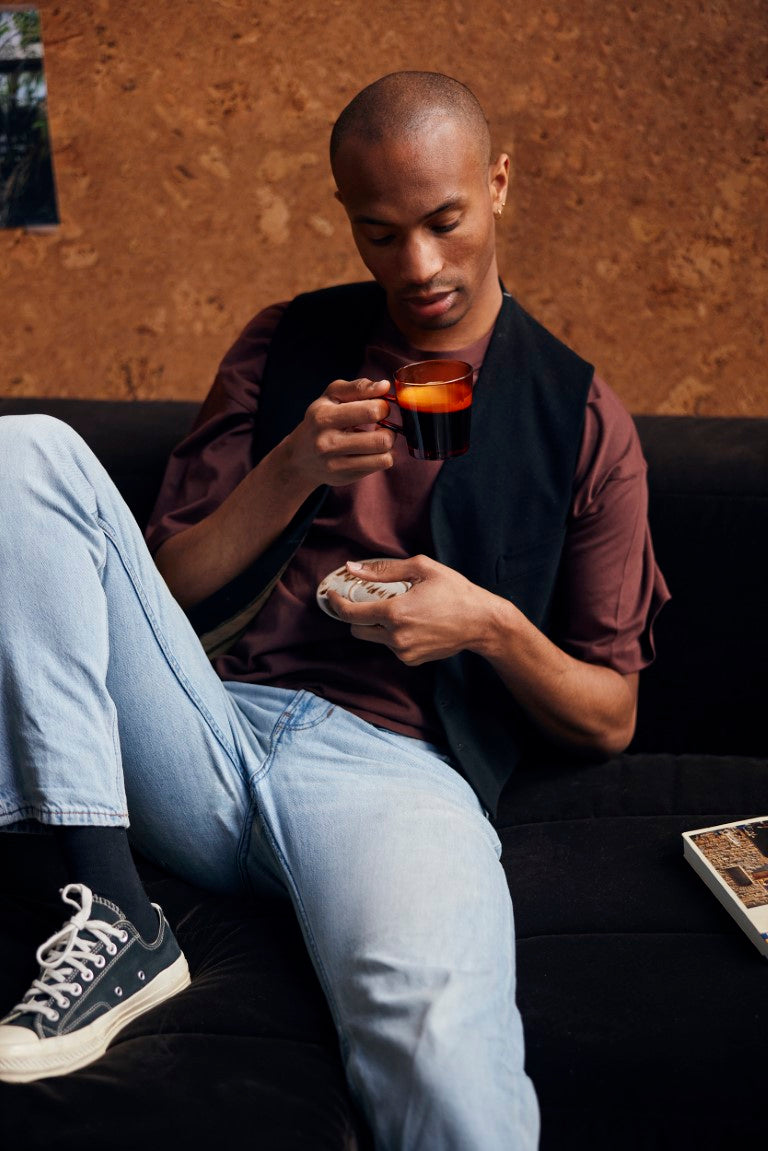 man wearing All Stars drinking coffee from  glass coffee cup