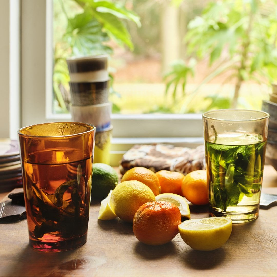 colored glass tall tumblers with hot mint tea oranges and lemons in front of window