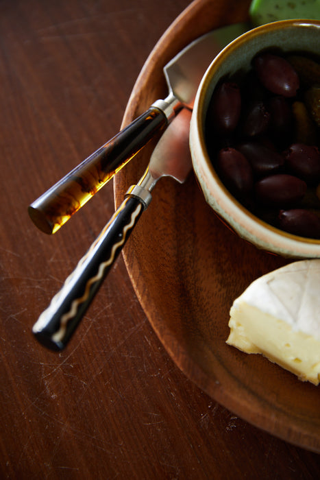 cheese knives on a wooden plate with brie and olives