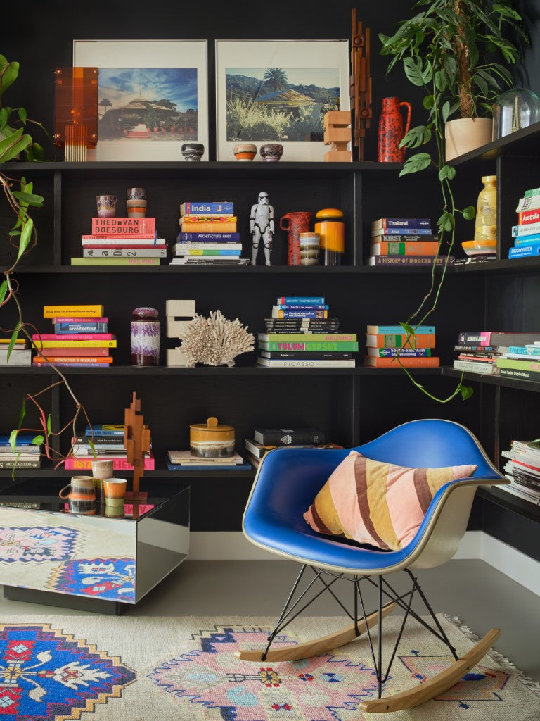 teak wooden skyline sculpture on a mirror block table in front of open shelving with books and ceramics