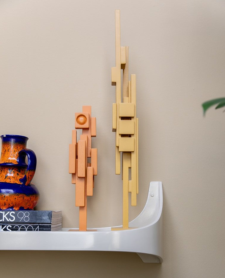 two wooden sculptures in orange and yellow on a white shelf