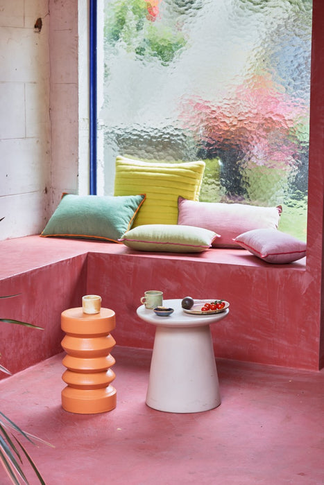 pink patio with green, yellow and pink pillows, earthenware side table and orange funky shaped accent table