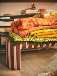 blush and maroon striped upholstered bench with fabric in bright colors stacked on top