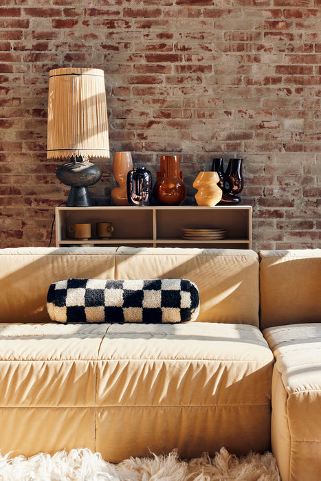 various flower vases against a brick exposed wall with a black and white bolster pillow on a cream colored velvet sofa