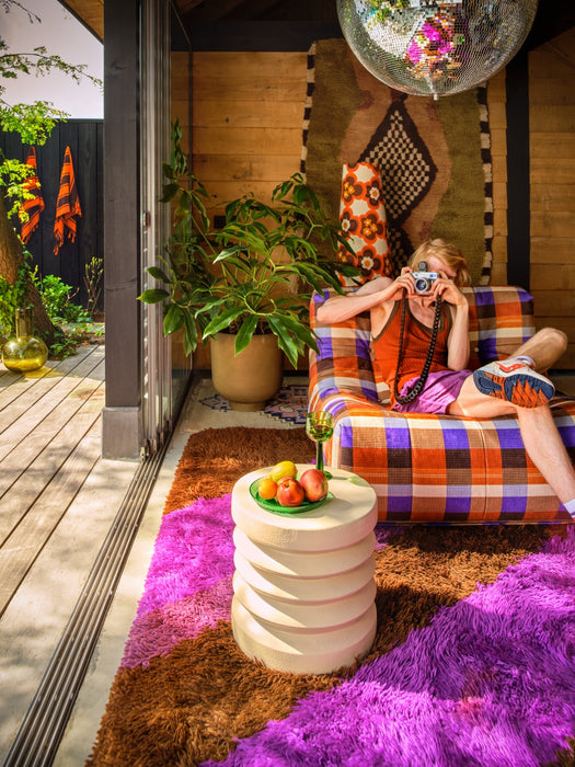 seating area with patterned lounge chair, purple and brown rug, woman taking a picture with old school photocamera