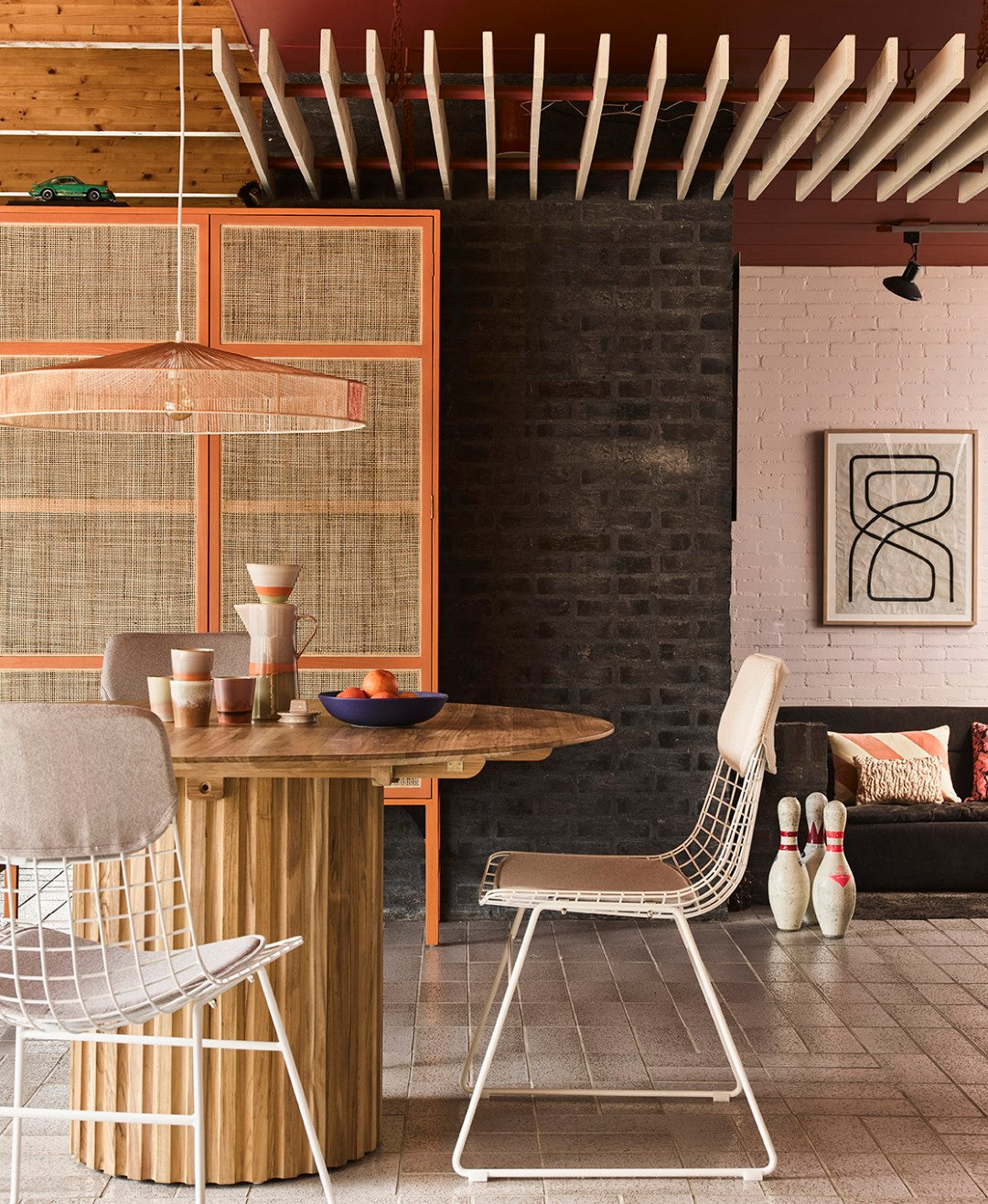 handwoven pendant rope lamp in terra shades hanging above a round teak wood dining table with white metal chairs