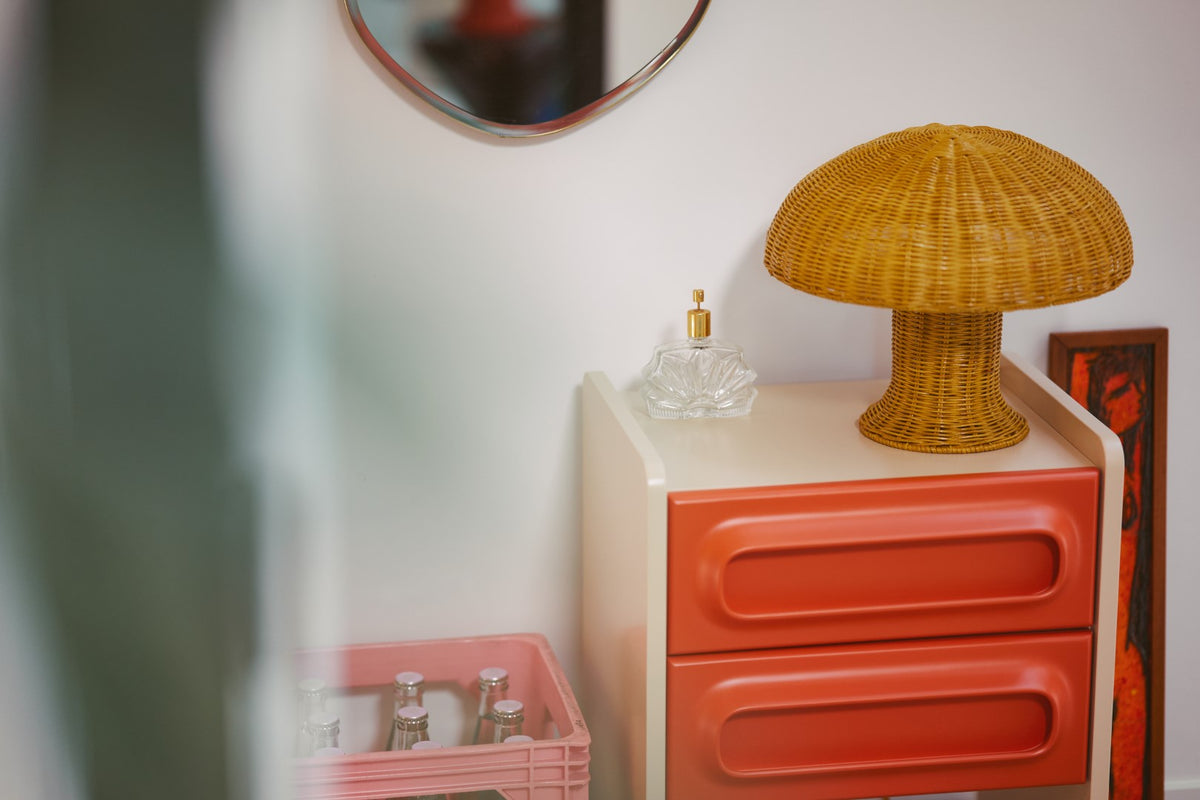 mustard yellow table lamp made from rattan on a nightstand with orange drawers