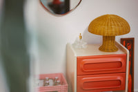 mustard yellow table lamp made from rattan on a nightstand with orange drawers