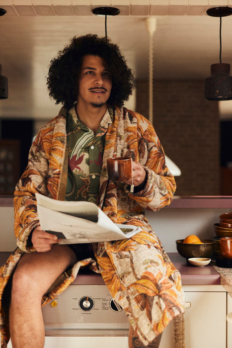 man drinking tea in bathrobe with pockets and orange brown palm tree motive