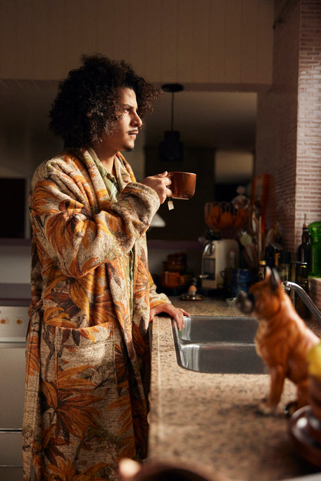 man drinking tea in bathrobe with pockets and orange brown palm tree motive