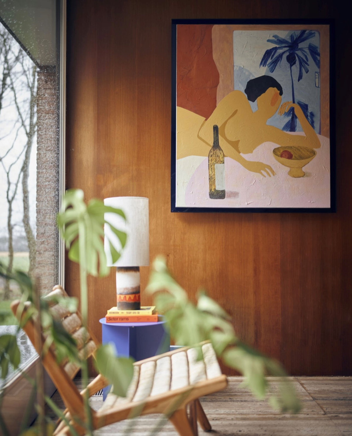 figurative painting of woman in a blue frame on a wooden wall with lounge chair and retro style table lamp