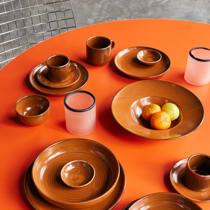 burned orange ceramic mug with ear on table with brown orange plates and pink tealights 
