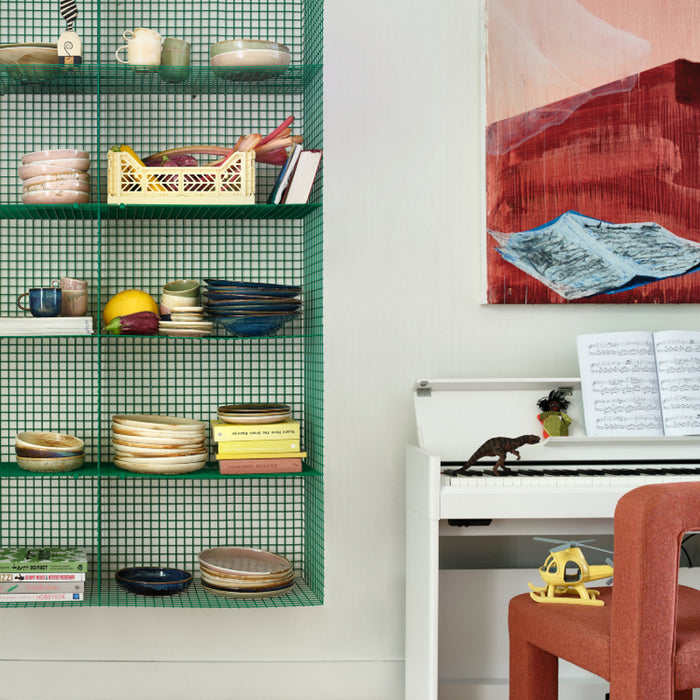 chef ceramics in different colors in green open shelving next to a white piano