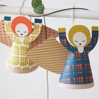 Colorful paper angels with patterned dresses hanging on a string.