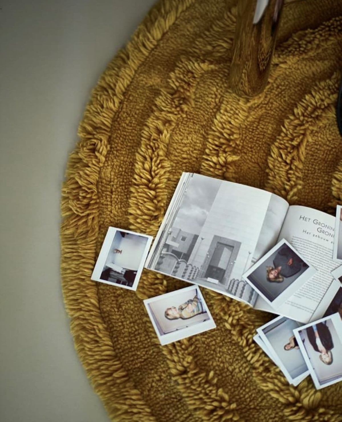 round rug with high and low poles in a greenish yellow color with polaroid's and a magazine