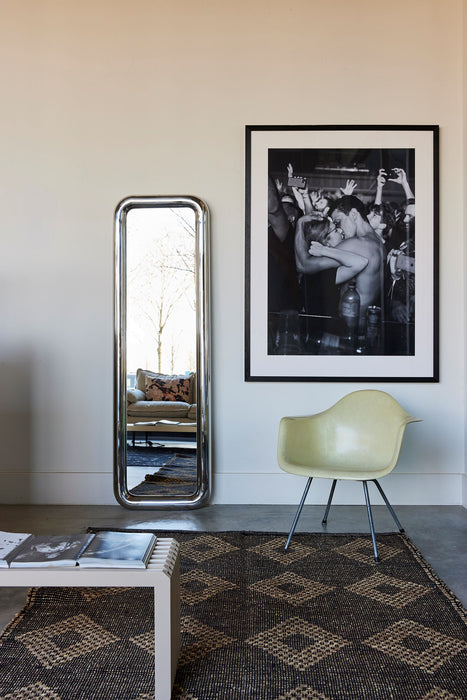 tall long standing chrome chubby mirror next to large black and white photo art in black frame
