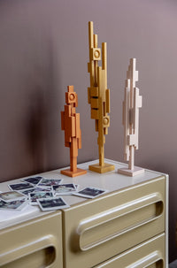 3 wooden skyline sculptures in orange, ochre and beige on a sideboard with polaroids