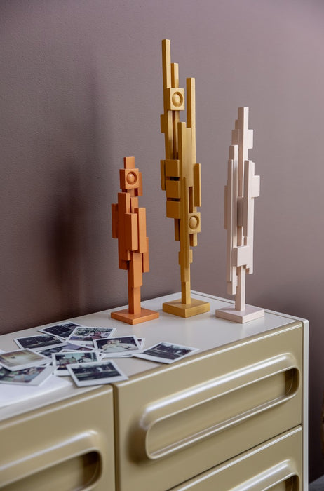 3 wooden skyline sculptures in orange, ochre and beige on a sideboard with polaroids