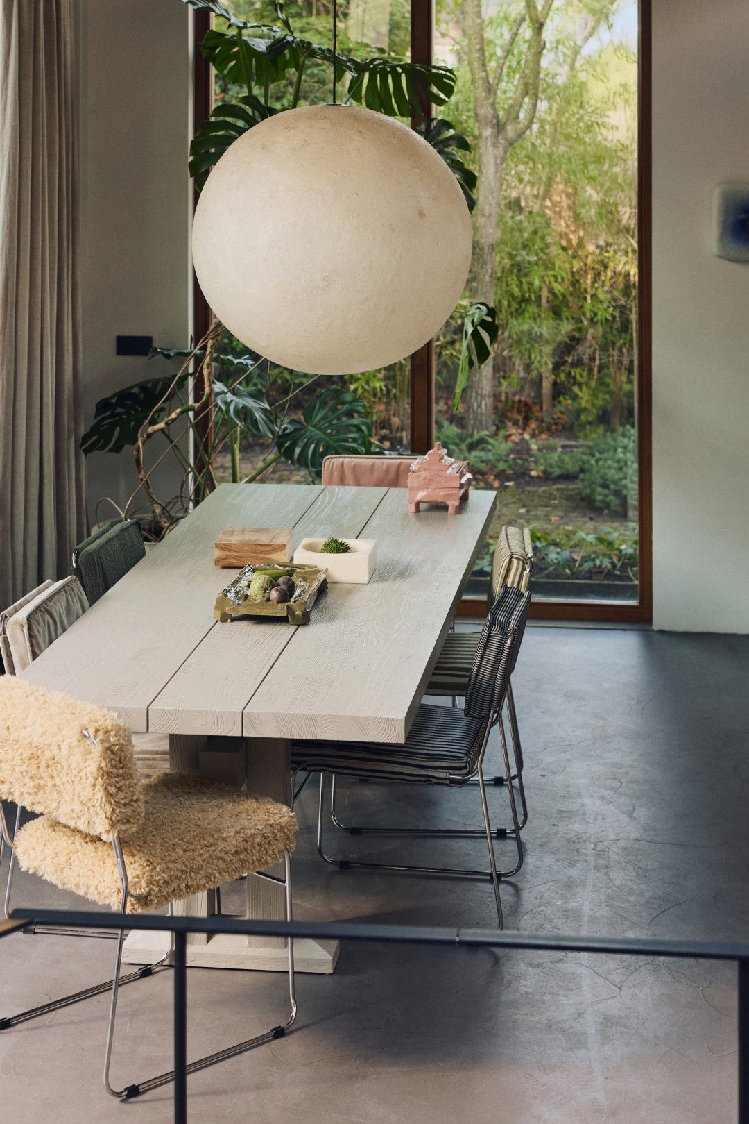 Dining area with a long table and chairs, large spherical light fixture, and garden view.