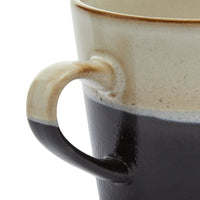 Close-up of a ceramic mug with a handle, showing a gradient from beige to black.