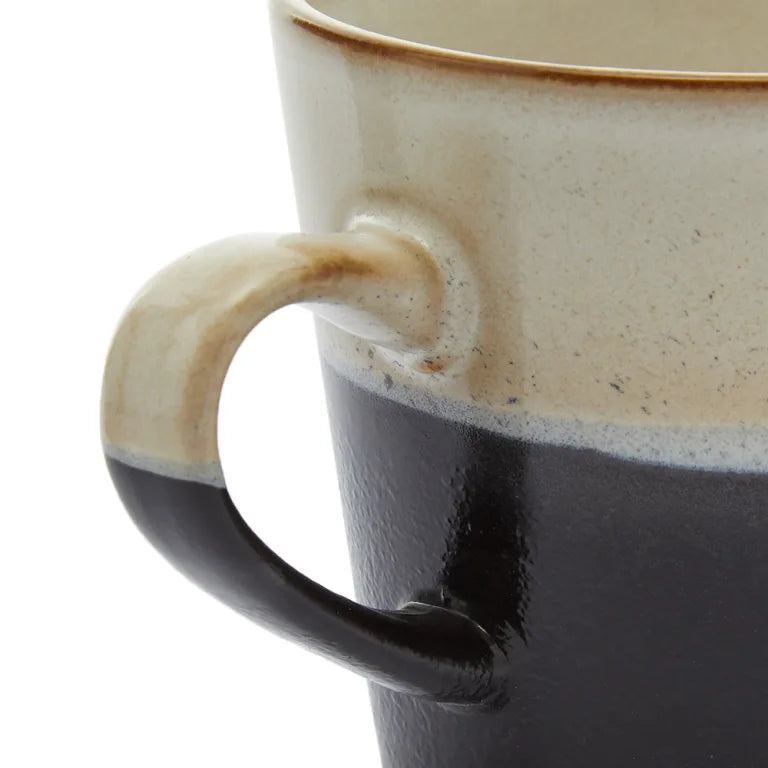Close-up of a ceramic mug with a handle, showing a gradient from beige to black.