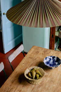 Wooden table with bowls containing pears and a decorative lampshade in a room.