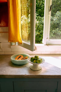 Kitchen counter with bowls of fruit near a window with yellow curtains