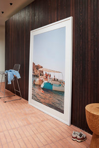 Framed photograph of a coastal scene on a wooden floor with a dark wooden wall.