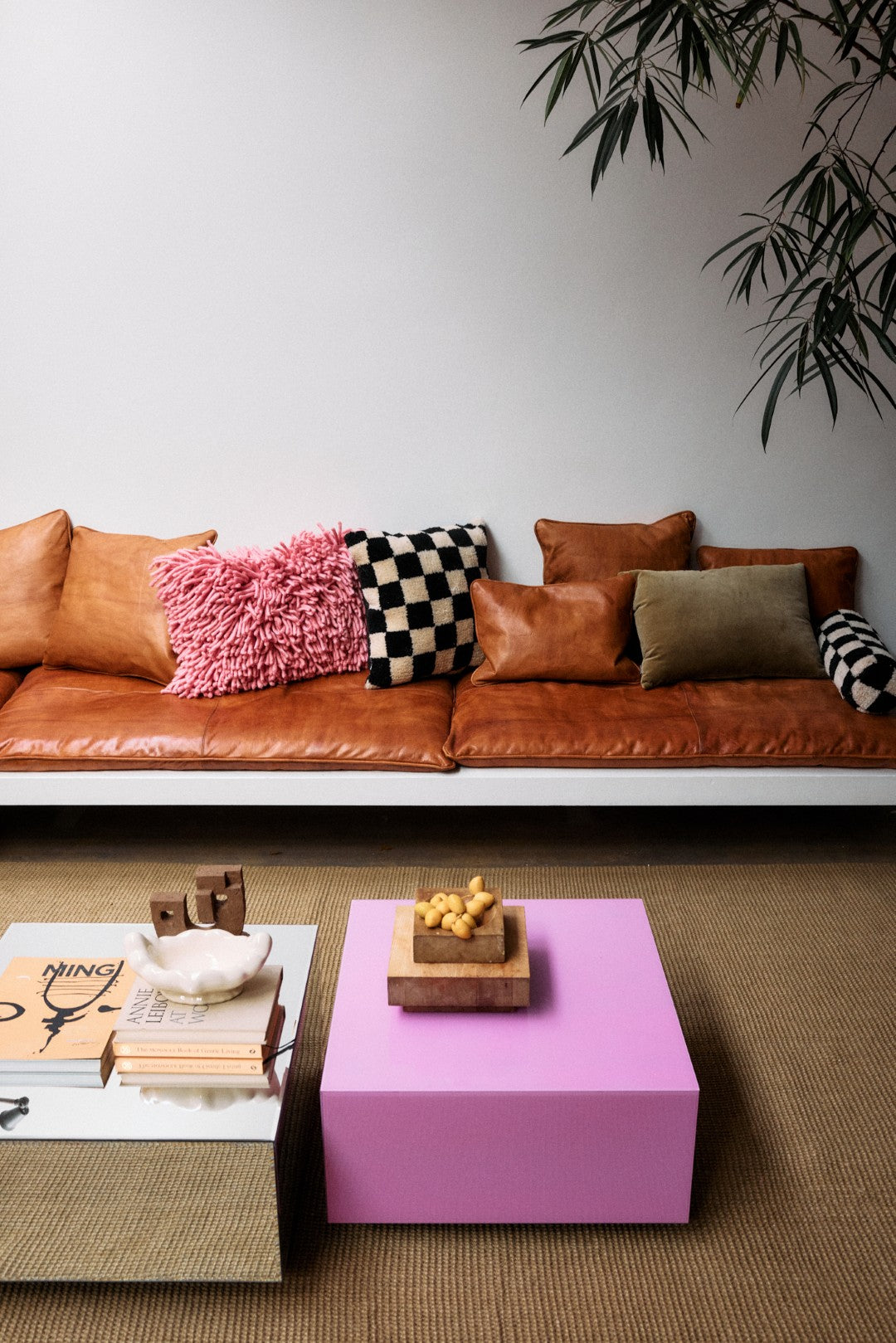 Brown leather sofa with colorful pillows and a pink coffee table in a living room.