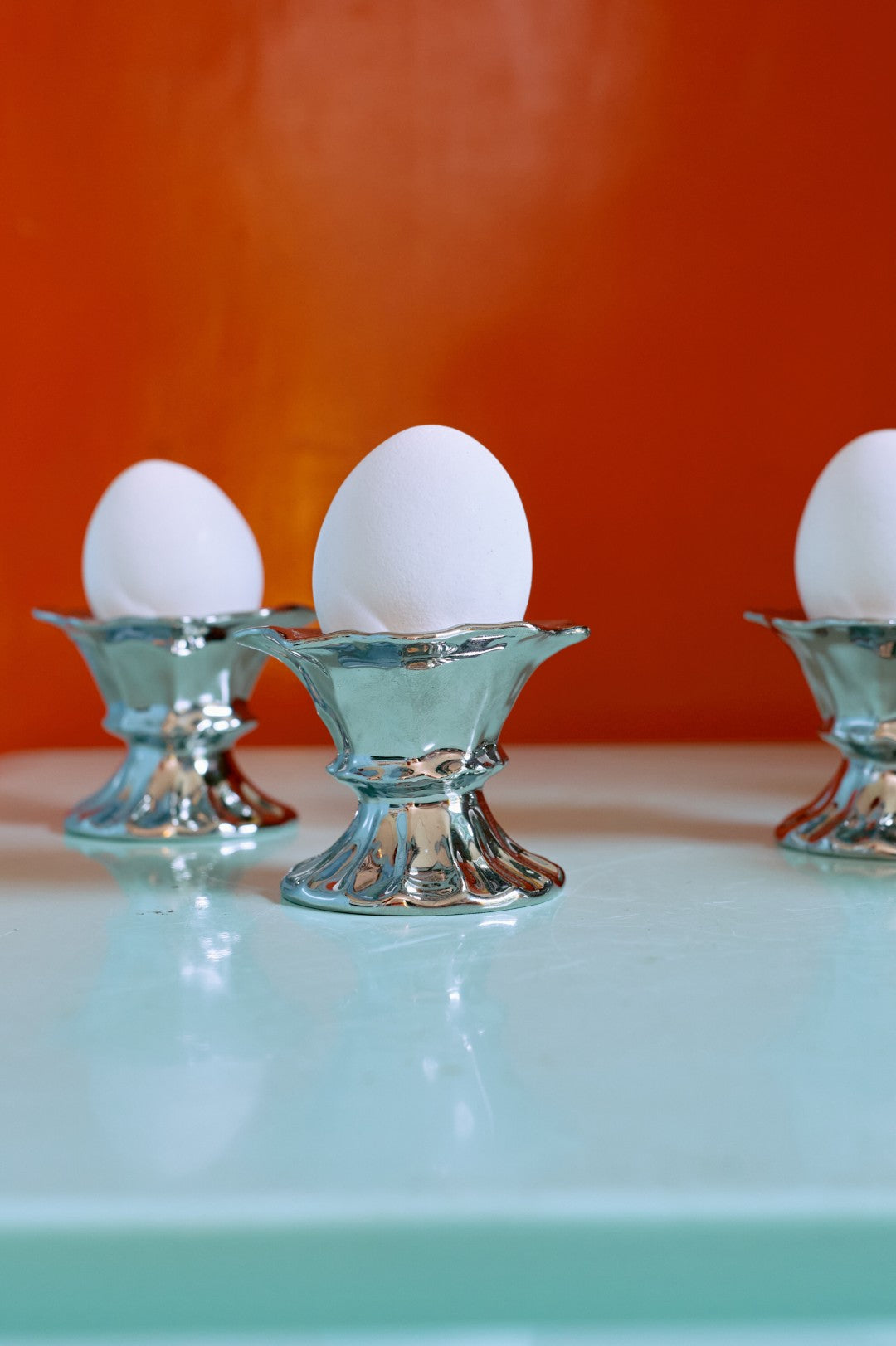 Three eggs in decorative stands on a light blue surface with an orange background