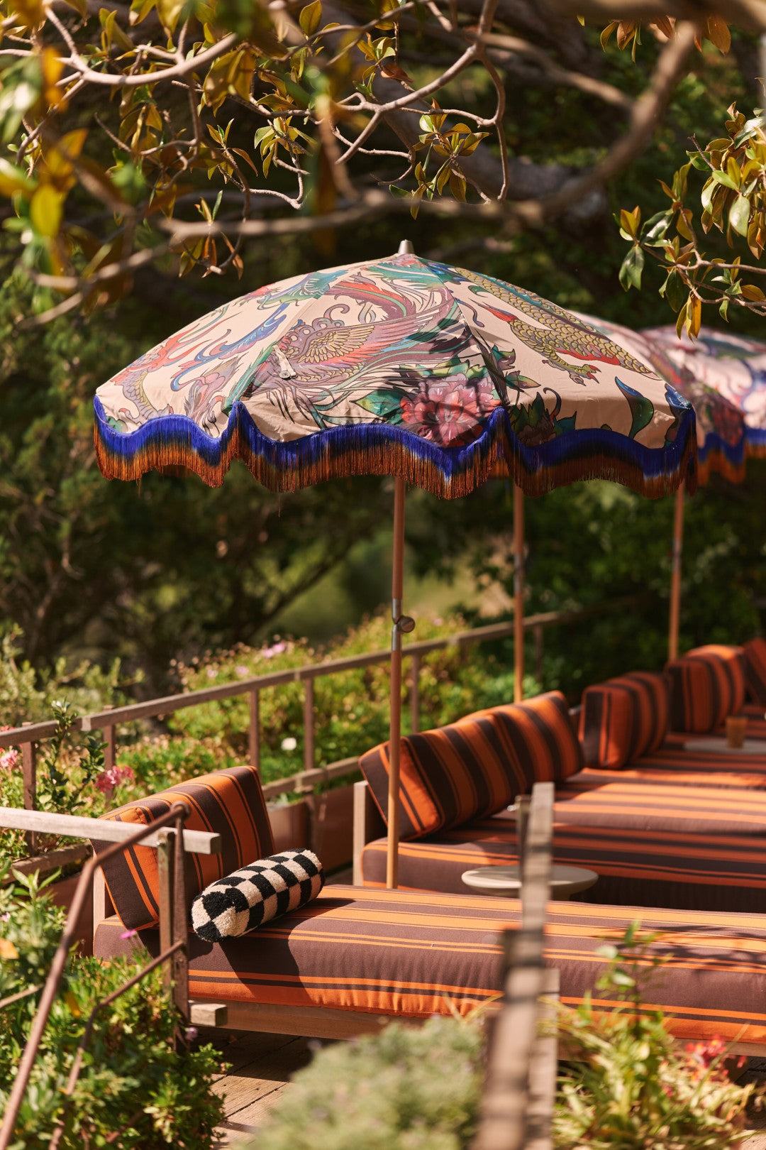 Outdoor lounge area with colorful umbrellas and striped cushions surrounded by greenery.