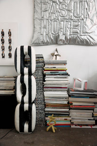 Black and white striped sculpture next to a stack of books with decorative items on a white wall.
