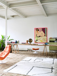 large painting of woman sitting with pink frame hanging in bright room with orange chair