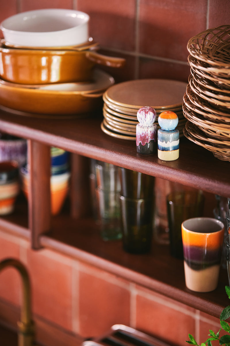 Stacks of ceramic plates and bowls on a wooden shelf with a tiled wall background.